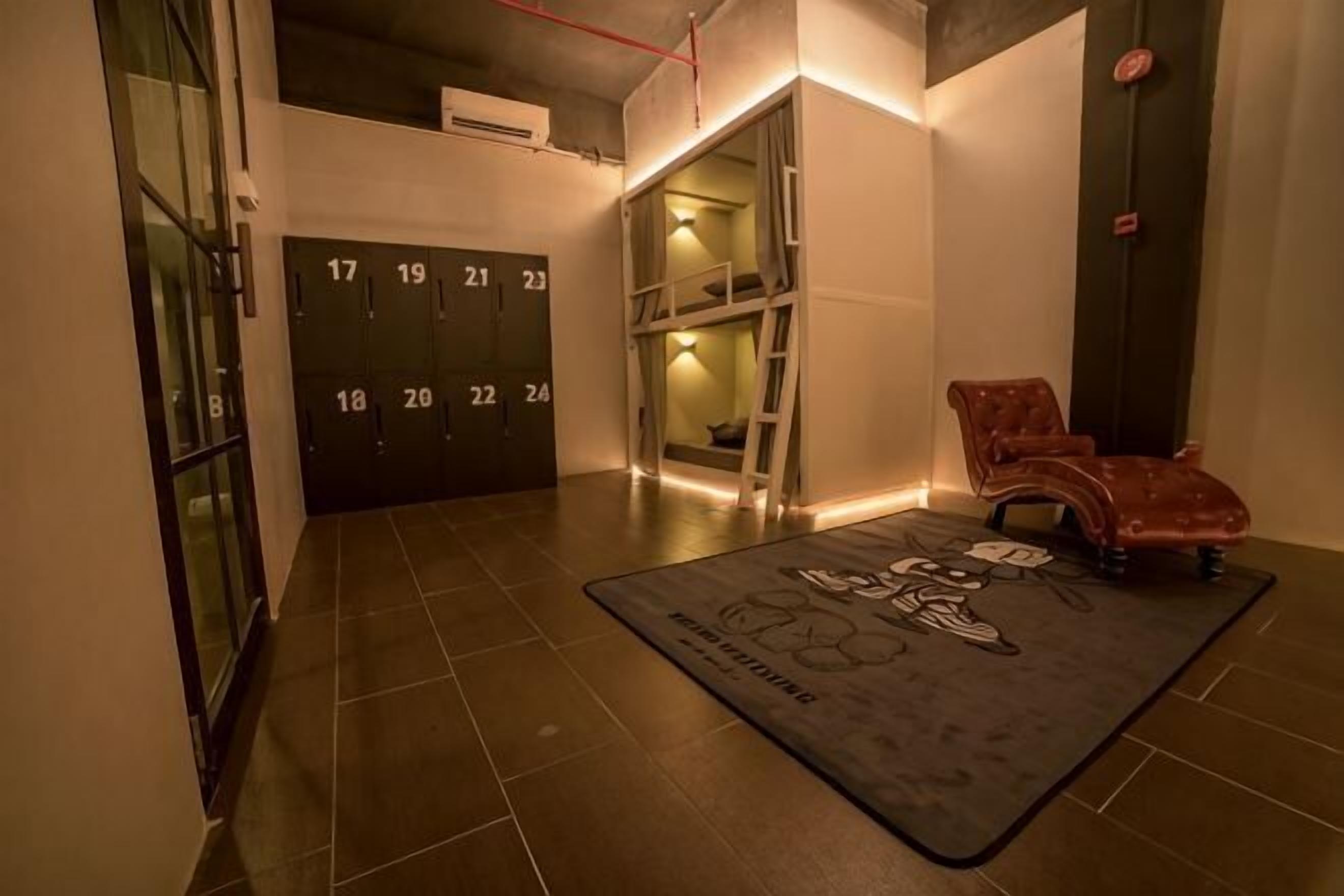 A hotel lobby with a tiled floor, numbered doors, a red leather chair, and a black and white rug.