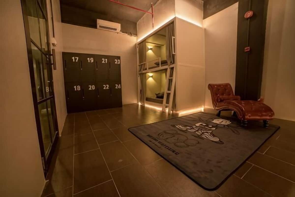 Un vestíbulo de hotel con suelo de baldosas, puertas numeradas, un sillón de cuero rojo y una alfombra blanco y negro.