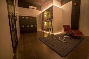 Een hotel lobby met een betegelde vloer, genummerde deuren, een rode leren fauteuil en een zwart-wit tapijt.