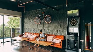 A modern lounge area with a sofa, a coffee table, a dartboard, and a bicycle mounted on the wall. - Bed Attitude Hostel Cenang (Langkawi)