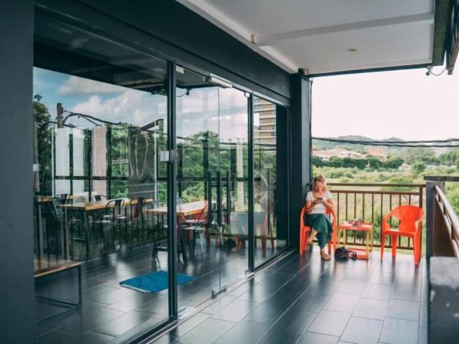 A balcony with a glass door leading to a dining area, a view of the countryside, and a person standing by the door.