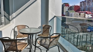 A balcony with wicker chairs and a table, overlooking a cityscape with buildings. - Libereco (Batumi)