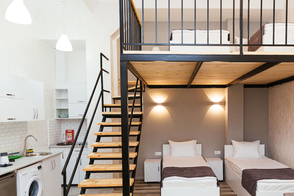 A compact hotel room with a bunk bed, a kitchenette, and a staircase leading to an upper level.