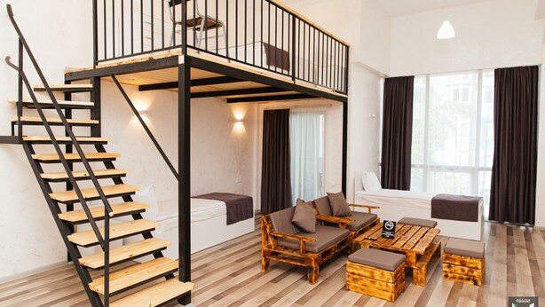 A loft-style room with a wooden staircase, a sofa set, and a dining table. - Libereco (Batumi)