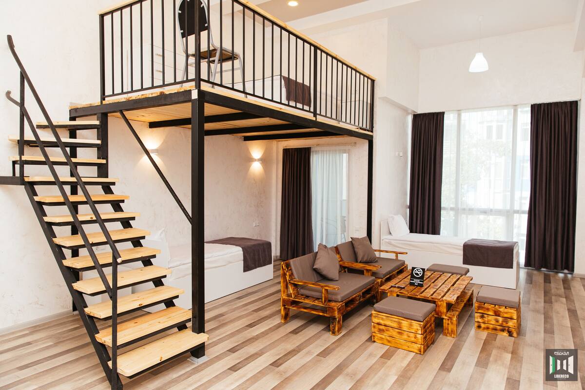 A loft-style room with a wooden staircase, a sofa set, and a dining table.