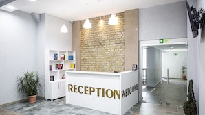 A reception area with a reception desk labeled "RECEPTION WELCOME," a stone wall, a potted plant, and a bookshelf. - Libereco (Batumi)