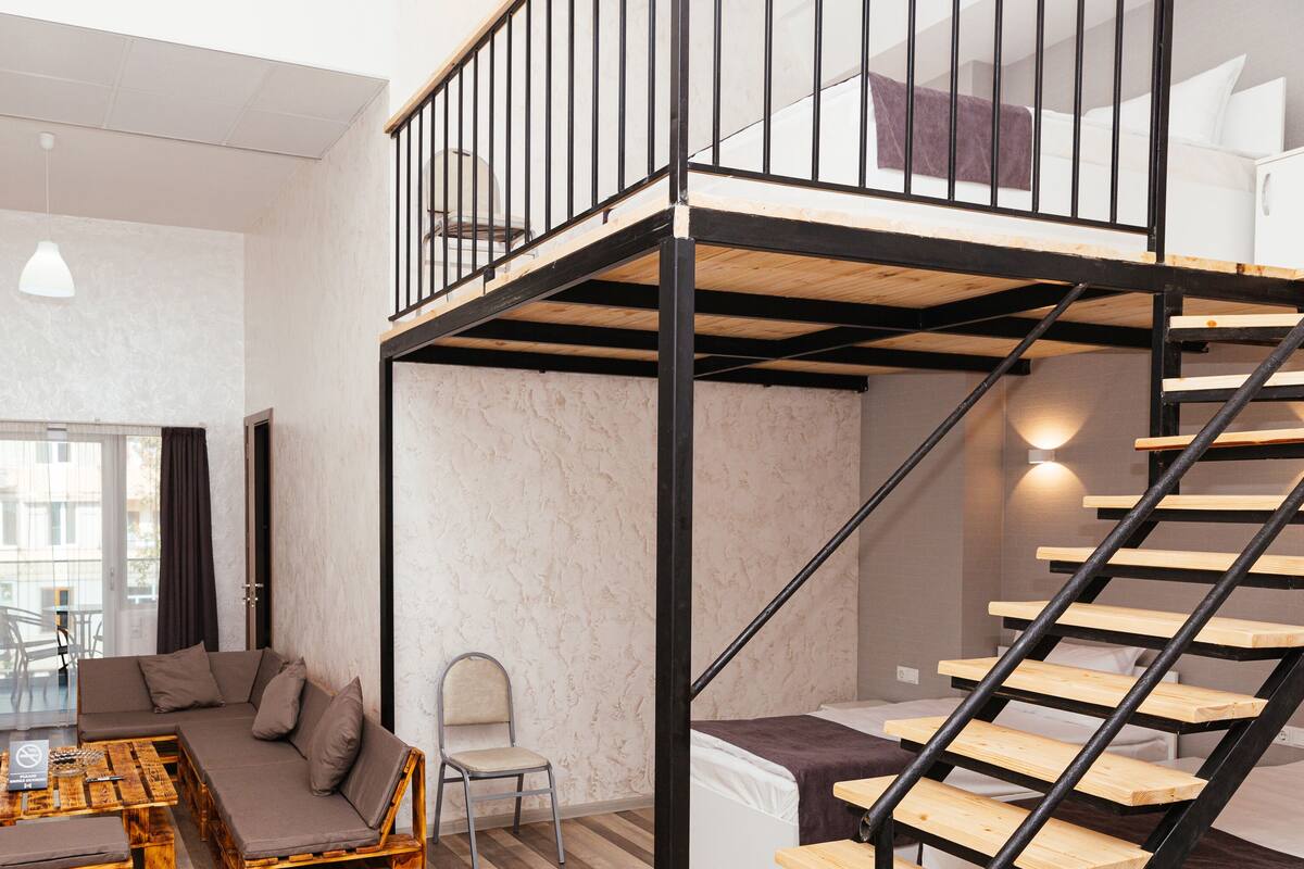 A modern interior with a loft bedroom, a sofa, a dining table, and a staircase.
