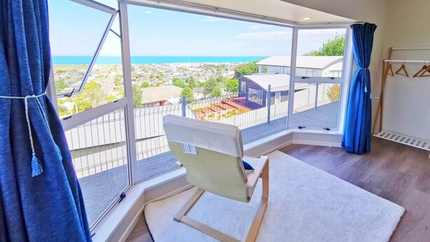 A balcony with a view of the sea and buildings, a chair, and a white rug.