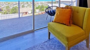 A yellow sofa with an orange pillow in a room with large windows overlooking a beach.