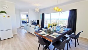 A modern dining area with a large table set for six, black chairs, and a view of the city through large windows.
