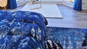 A bedroom with a large window, a bed, a chair, and a view of the landscape.