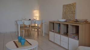 Et spiseområde med et bord og stole, et lille rundt bord med blå krus, et skab med dekorative genstande, og en vægmonteret lampe.