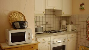 Uma cozinha compacta com armários brancos, micro-ondas, torradeira, cafeteira e fogão a gás.