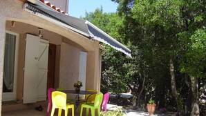 Um pátio com mesa, cadeiras, um vaso de planta e um edifício com porta e janelas.