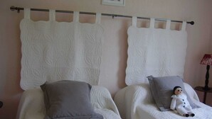 Duas camas de solteiro com roupa de cama branca e cabeceira decorativa.