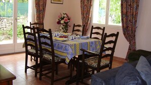 Uma área de refeições com uma mesa posta para quatro pessoas, rodeada por cadeiras de madeira.