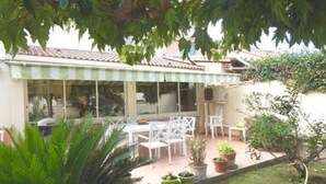Eine Terrasse mit weißen Stühlen und Tischen, umgeben von Blumentöpfen und einem kleinen Garten.