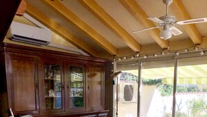 Ein Wohnzimmer mit einem Holzschrank, zwei gemusterten Sesseln, einem Deckenventilator und einem Esstisch mit Stühlen.