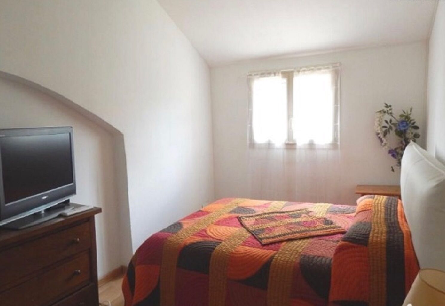 A bedroom with a bed, a television on a dresser, and a window with curtains.