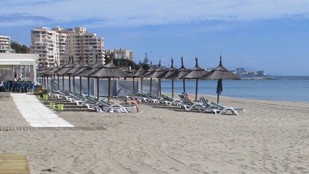 A beach with sun loungers and umbrellas, a wooden boardwalk, and buildings in the background. - Villa Chispita (Fuengirola)