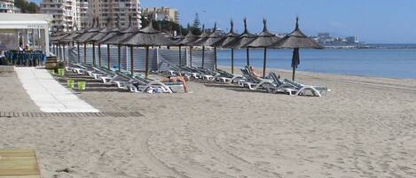 Pantai di sekitar, pasir putih, kursi berjemur, dan payung pantai