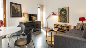 Un salon moderne avec une table blanche, des chaises noires, un canapé gris, une table basse en bois et un téléviseur posé sur un meuble noir.