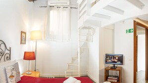 Une chambre d’hôtel avec un lit rouge, un climatiseur blanc, une télévision, une bibliothèque et un escalier.