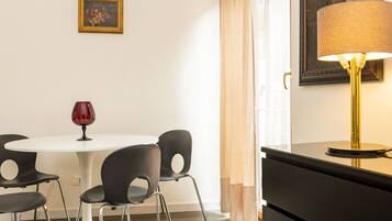 Zona pranzo con tavolo rotondo, quattro sedie, un bicchiere da vino rosso, una lampada e un quadro appeso al muro.