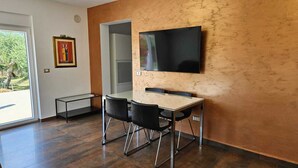 A modern dining area with a table and chairs, a flat-screen TV mounted on the wall, and a door leading to an outdoor area.