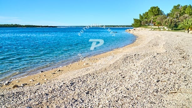 A pebbly beach with clear blue water and a distant shoreline.
