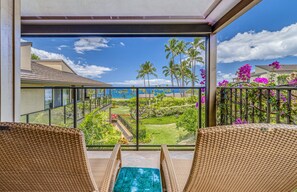 A balcony with wicker chairs and a view of a landscaped garden and ocean.