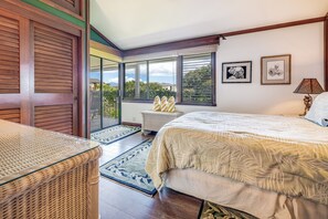 A bedroom with a large bed, a wicker chair, a small table, and a view of the outdoors through a sliding glass door.