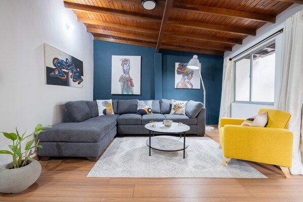 Un salon moderne avec un canapé d’angle gris, un fauteuil jaune et une table basse ronde.