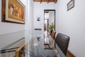 Um corredor com uma mesa de vidro, cadeiras e quadros nas paredes.