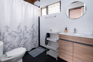 Une salle de bain avec des toilettes, un rideau de douche à motifs floraux, un lavabo blanc avec un meuble-vasque en bois et un miroir au mur.