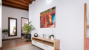 A room with a wooden floor, a white wall, a wooden console table with drawers, a large framed painting, and a potted plant. - Light-filled Envigado, top-floor w/ Large Patio (Envigado)