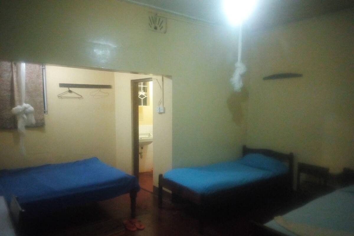 A small, dimly lit room with two single beds, a wooden door, and a hanging light fixture.