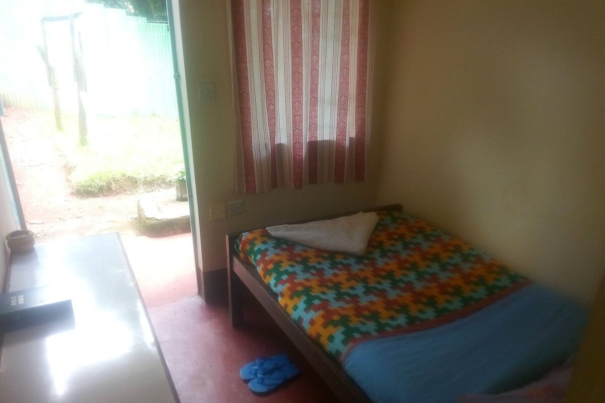 A small, simple room with a bed, a table, and a window.