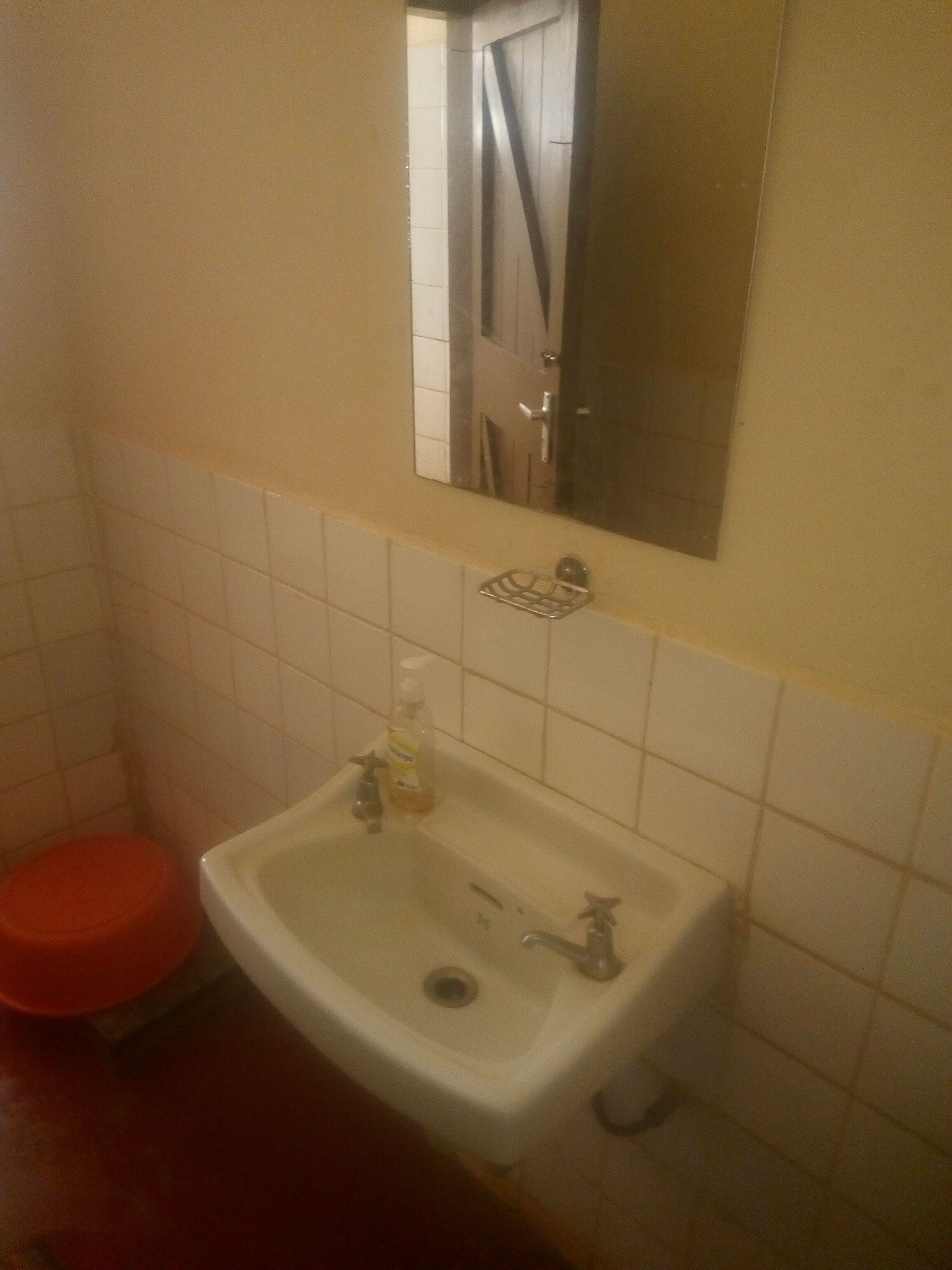 Un baño con un lavamanos blanco, un espejo encima y un inodoro rojo.