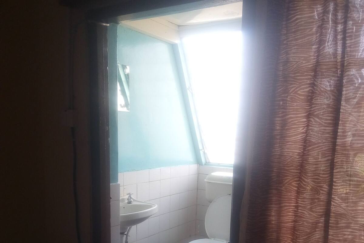 A bathroom with a white sink, toilet, and a small window with curtains.