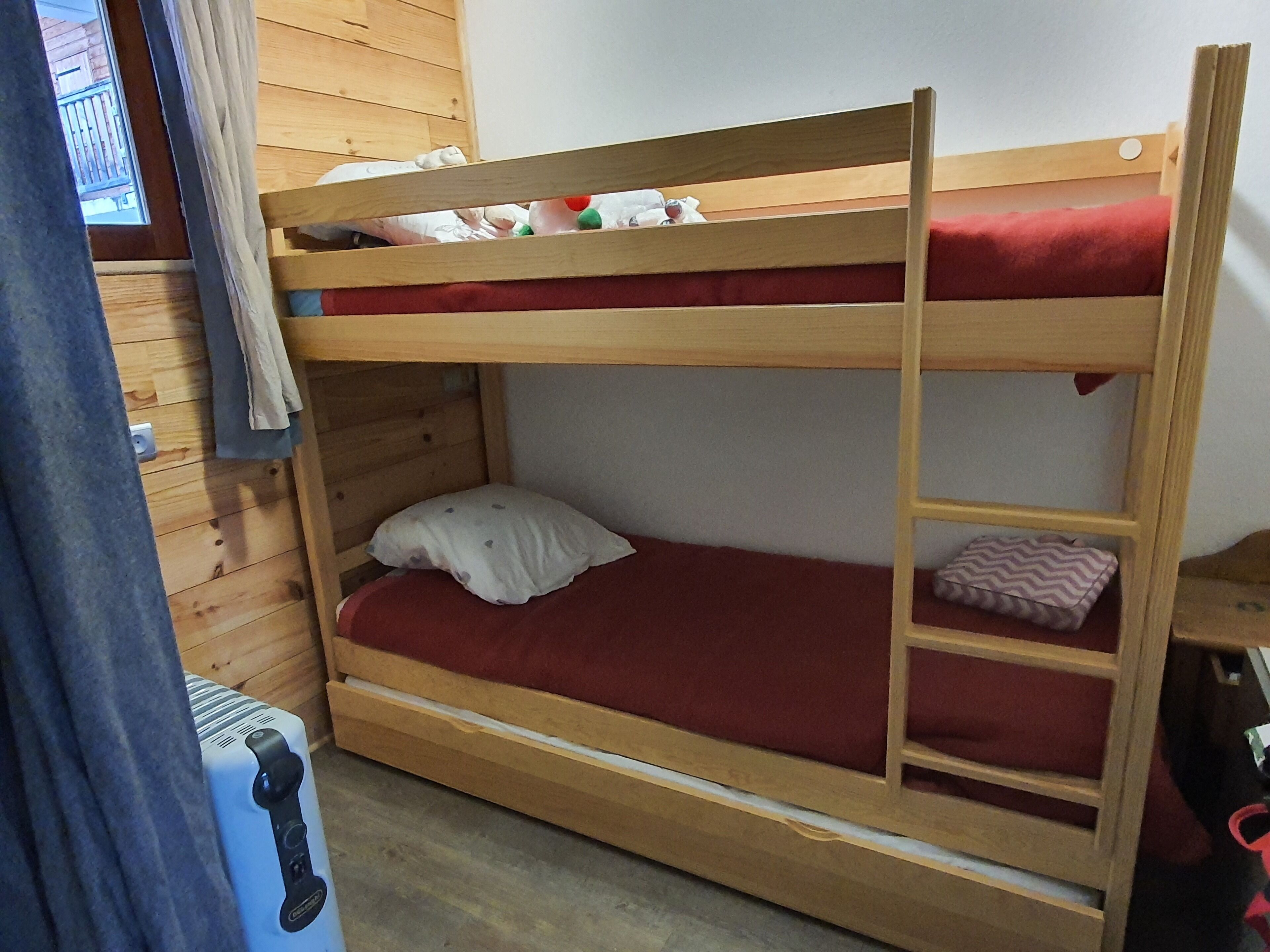 A bunk bed with a wooden frame, red bedding, and a small shelf.