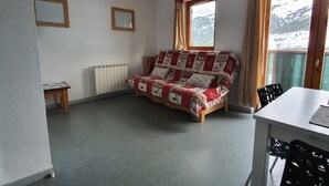 A cozy room with a wooden sofa, a small table, a radiator, and a window with a view of mountains. - Rental in the Mountain at Saint François LONGCHAMPS (Saint François LONGCHAMPS)