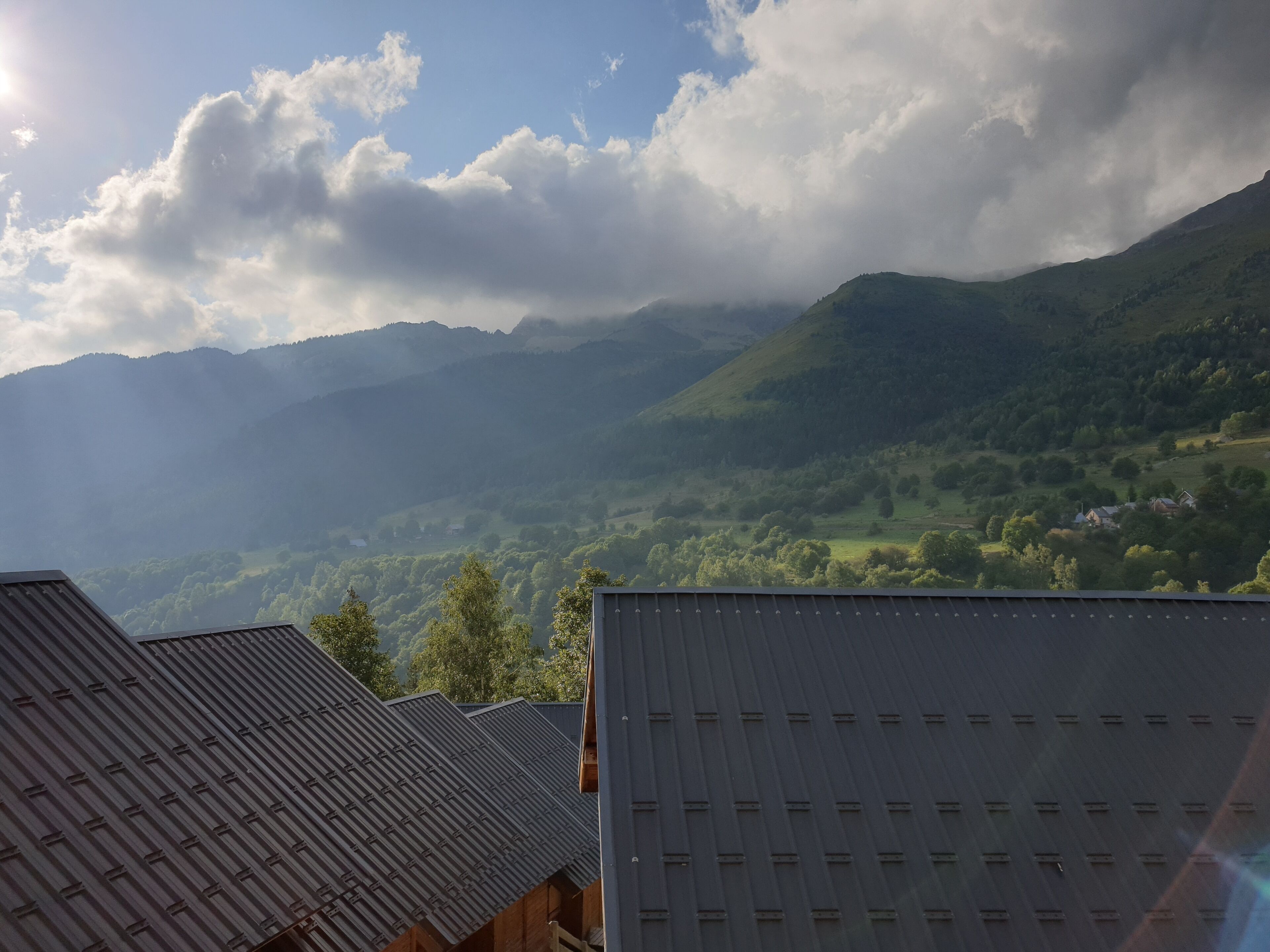 A view of a valley with mountains in the background and buildings with metal roofs in the foreground.