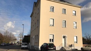 Um edifício com vários andares, fachada plana, diversas janelas e área de estacionamento com carros.