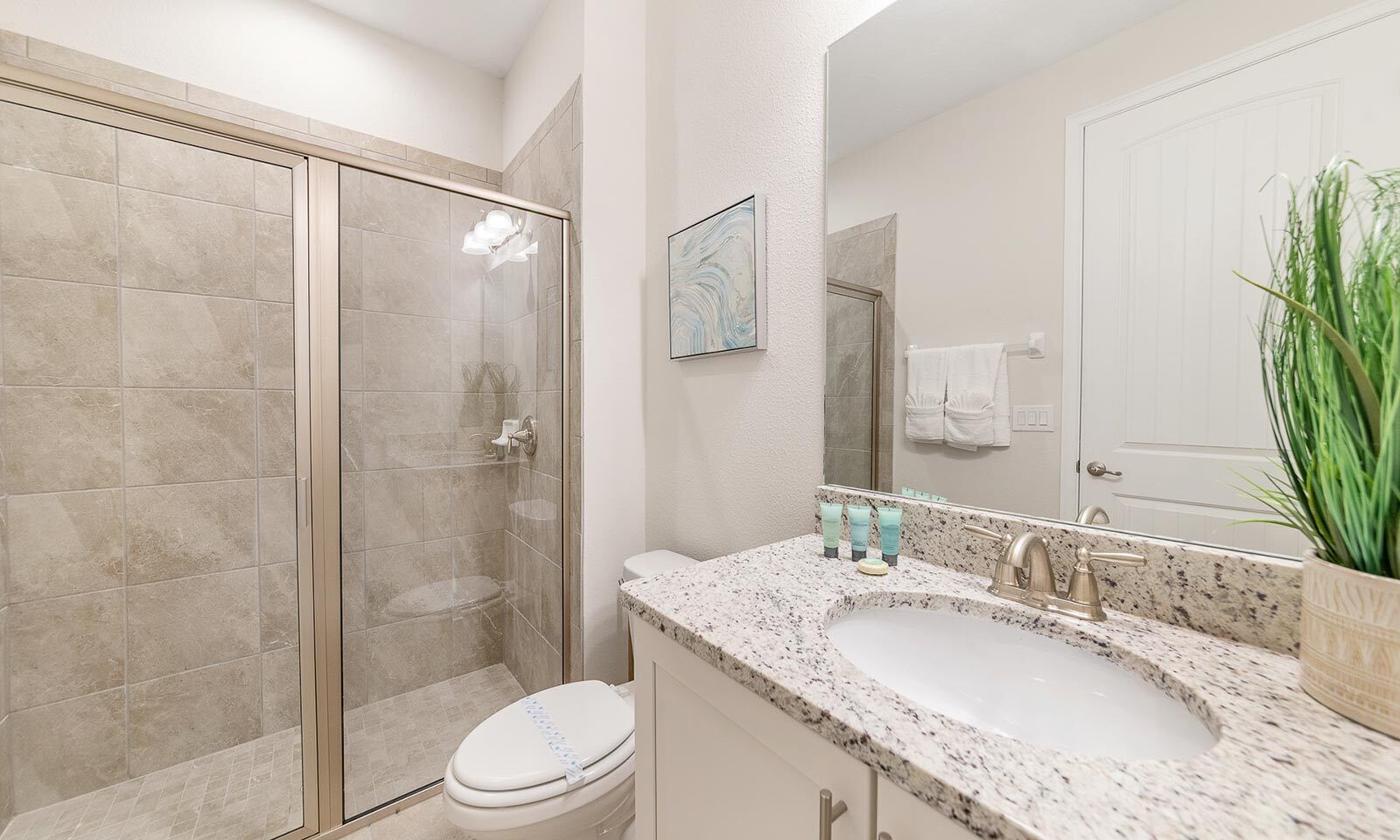 A bathroom with a glass shower enclosure, a sink with a granite countertop, and a toilet.