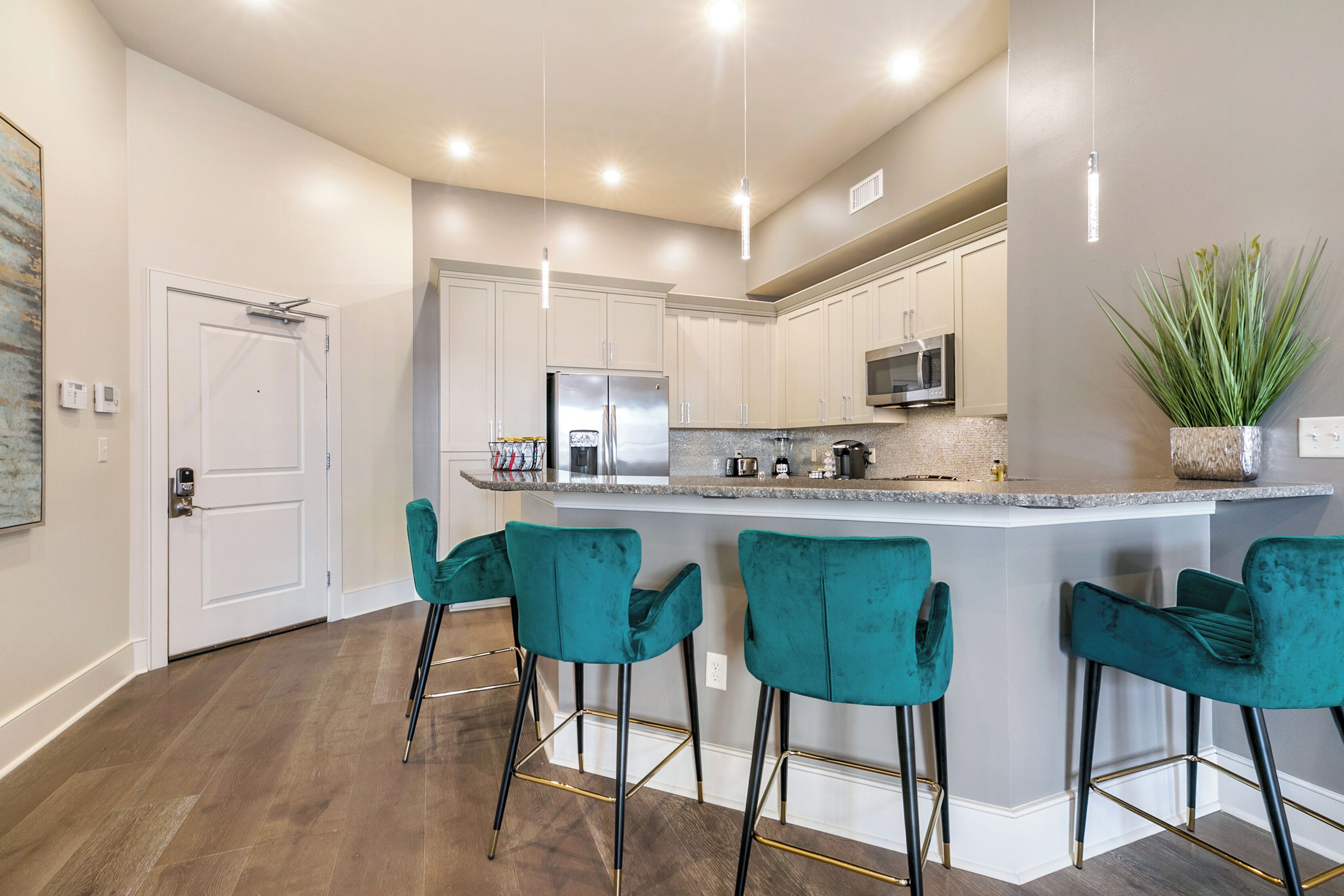 A modern kitchen with a central island, bar stools, stainless steel appliances, and pendant lighting.