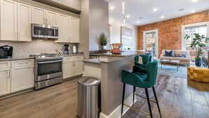 A modern kitchen with stainless steel appliances, a central island with bar stools, and a brick wall.
