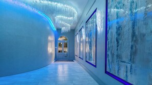 A hallway with a blue-lit wall, a chandelier, and framed artwork.