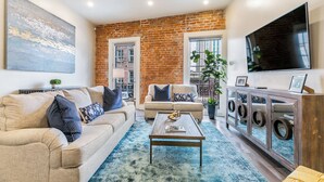 A living room with a brick wall, a large TV, a sofa, a coffee table, and a cabinet with circular mirrors.