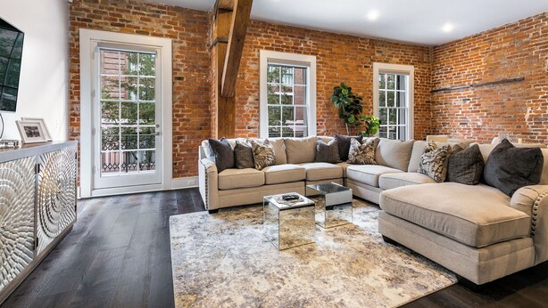 A spacious living room with a brick wall, large windows, and a sectional sofa.